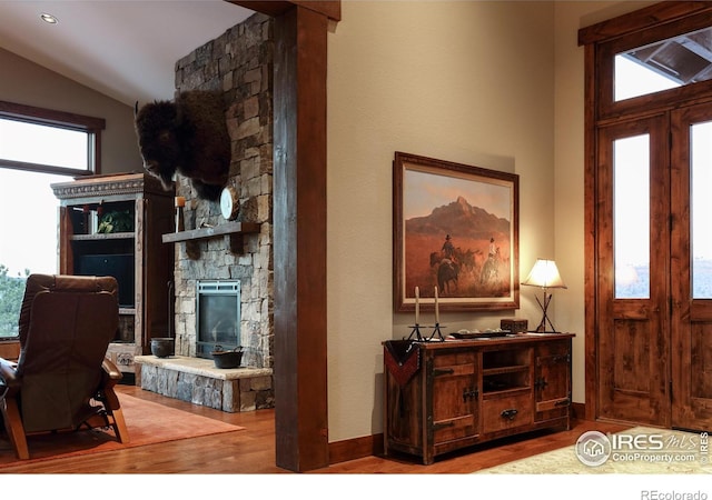 entryway featuring hardwood / wood-style flooring, vaulted ceiling, and a stone fireplace