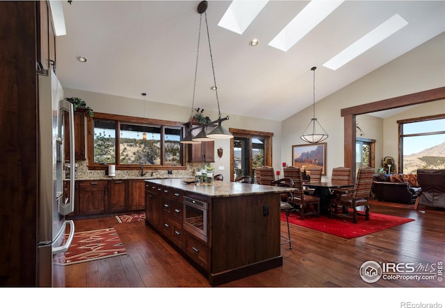 kitchen featuring a breakfast bar, a skylight, a center island, stainless steel appliances, and light stone countertops