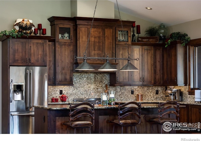 kitchen with light stone counters, decorative backsplash, stainless steel fridge with ice dispenser, and a breakfast bar area