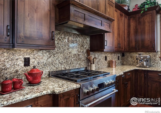 kitchen with tasteful backsplash, stainless steel range, light stone countertops, and custom range hood