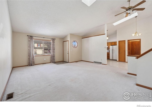 unfurnished living room featuring ceiling fan, light colored carpet, vaulted ceiling with skylight, and a textured ceiling