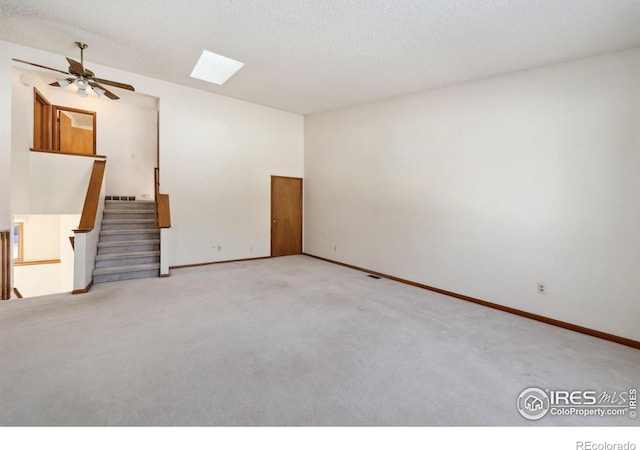 carpeted empty room with ceiling fan, a skylight, and a textured ceiling