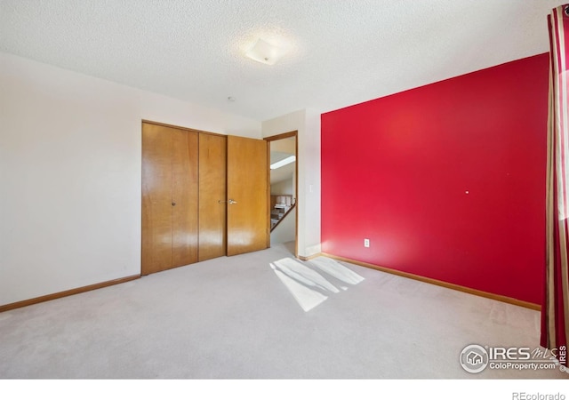 unfurnished bedroom featuring light carpet, a closet, and a textured ceiling