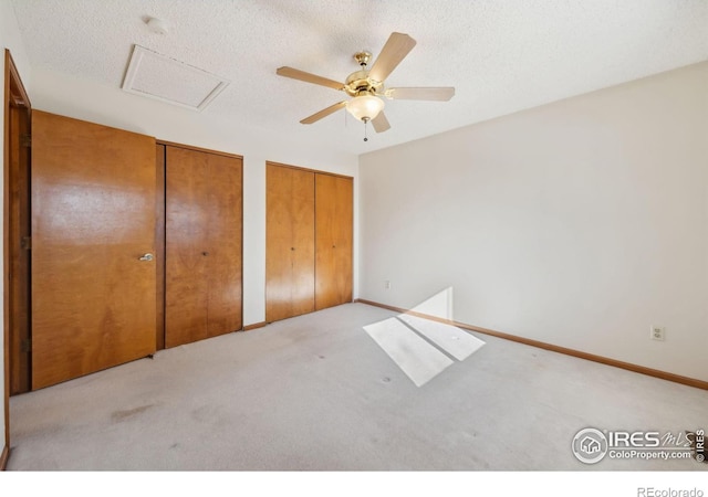 unfurnished bedroom featuring ceiling fan, light carpet, two closets, and a textured ceiling