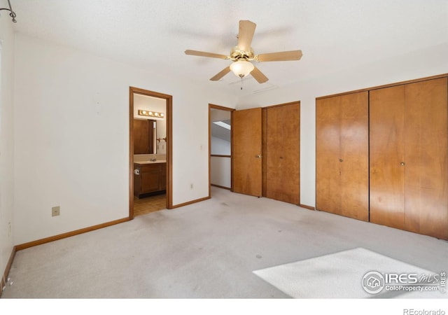 unfurnished bedroom with ceiling fan, ensuite bath, light carpet, and two closets