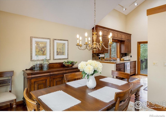 dining space with hardwood / wood-style floors, a notable chandelier, high vaulted ceiling, and rail lighting