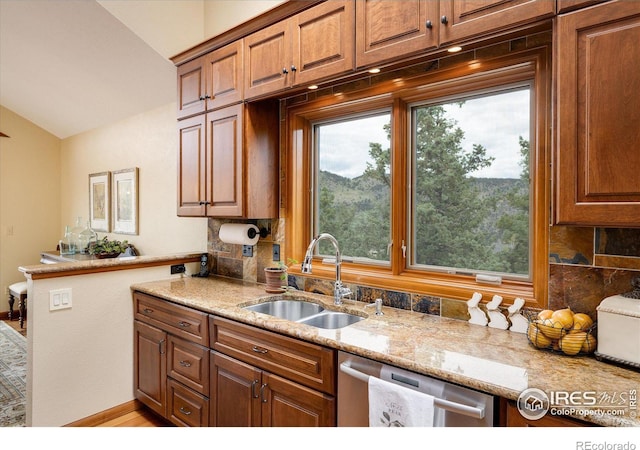 kitchen with vaulted ceiling, dishwasher, sink, backsplash, and light stone counters