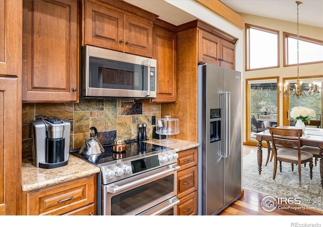 kitchen with light stone counters, an inviting chandelier, decorative light fixtures, appliances with stainless steel finishes, and decorative backsplash