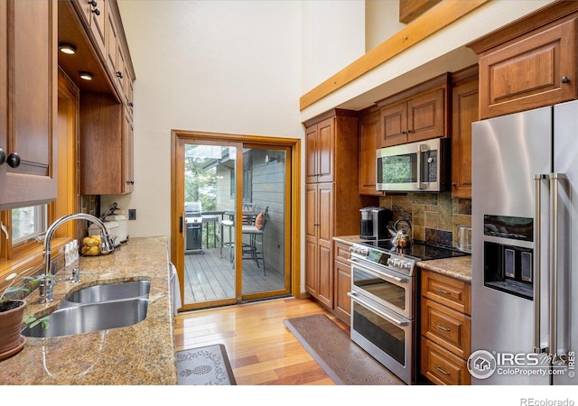 kitchen with sink, stainless steel appliances, light stone countertops, a healthy amount of sunlight, and light hardwood / wood-style flooring