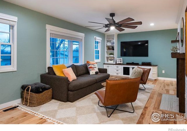 living room with built in shelves, ceiling fan, and light hardwood / wood-style flooring