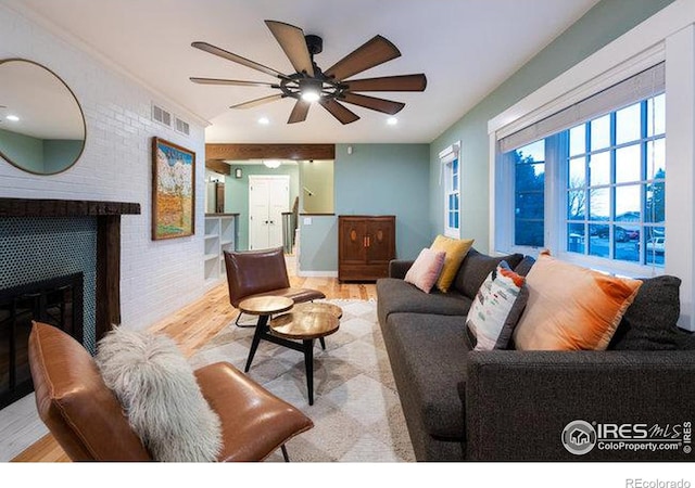 living room with ceiling fan, a brick fireplace, and light hardwood / wood-style flooring