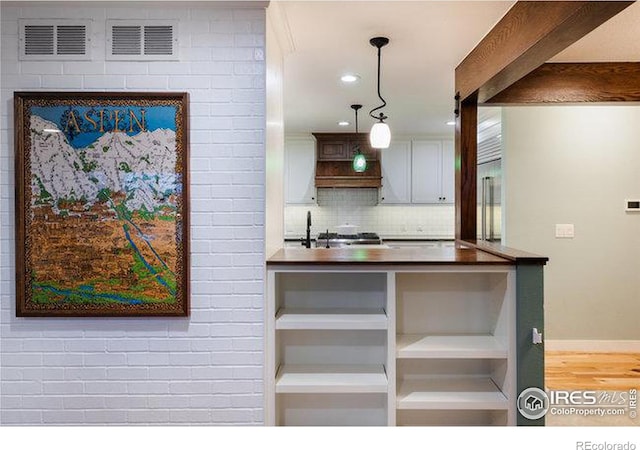 kitchen with sink, white cabinetry, hanging light fixtures, wood-type flooring, and decorative backsplash