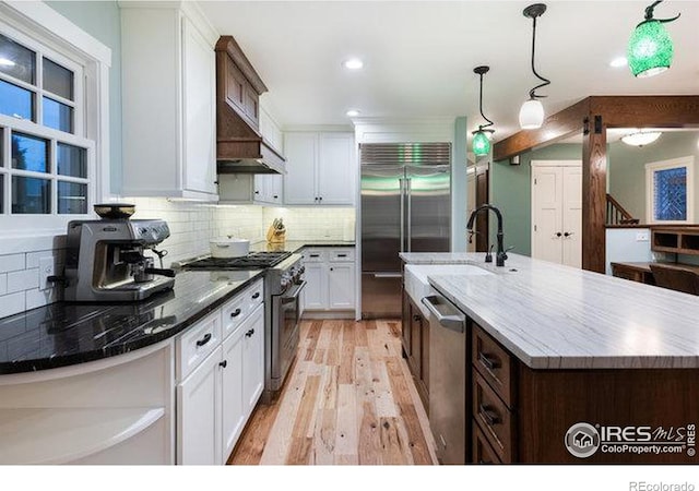 kitchen with pendant lighting, white cabinetry, an island with sink, sink, and high end appliances