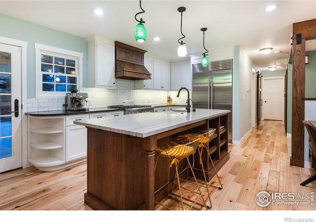 kitchen featuring sink, white cabinets, backsplash, hanging light fixtures, and a kitchen island with sink