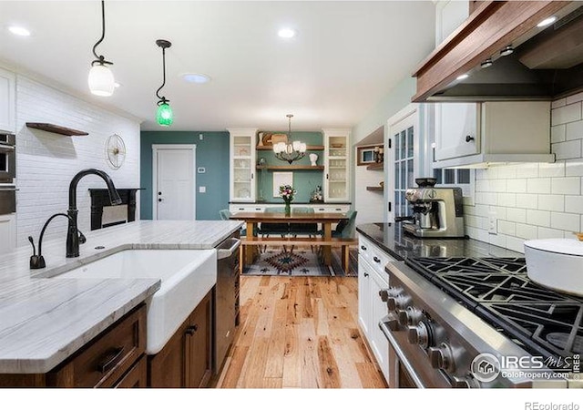 kitchen with premium range hood, appliances with stainless steel finishes, decorative light fixtures, dark stone countertops, and white cabinets