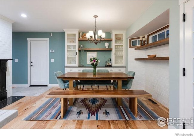 dining room with hardwood / wood-style flooring, a large fireplace, and a notable chandelier