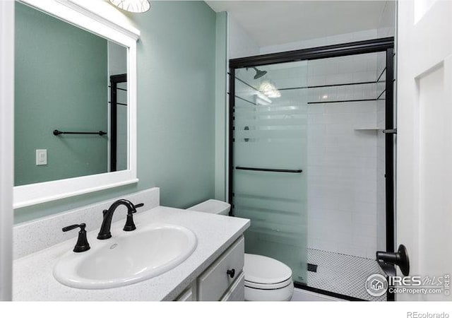 bathroom featuring a shower with door, vanity, and toilet