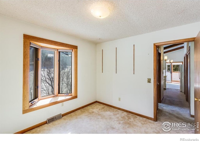 carpeted empty room featuring a notable chandelier and a textured ceiling