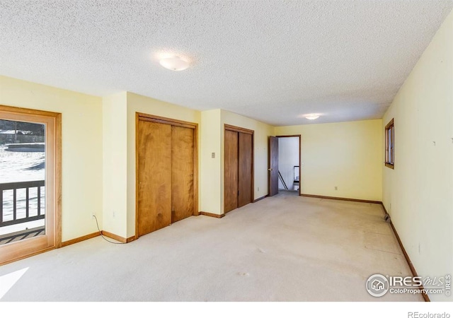 unfurnished bedroom featuring multiple closets, light colored carpet, and a textured ceiling