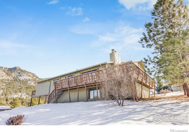 snow covered back of property featuring a garage and a wooden deck