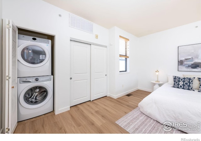 laundry area featuring stacked washer / dryer and light hardwood / wood-style floors