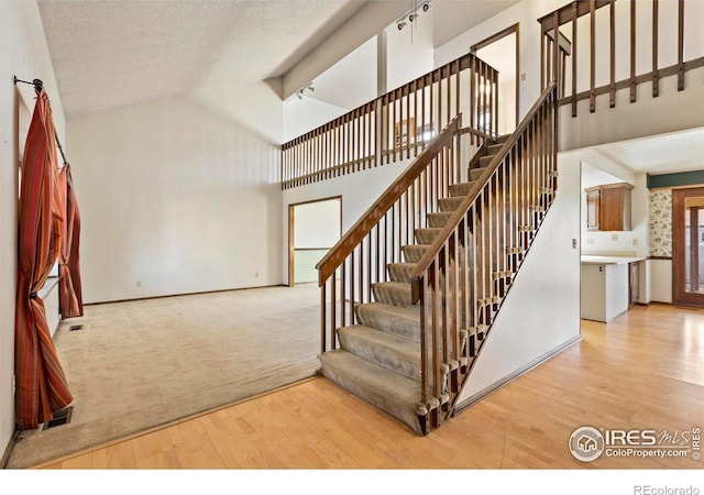 stairs featuring hardwood / wood-style floors, high vaulted ceiling, and a textured ceiling