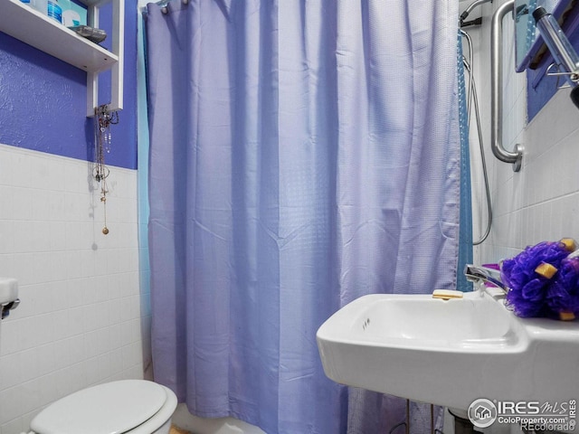 bathroom featuring a shower with curtain, toilet, sink, and tile walls