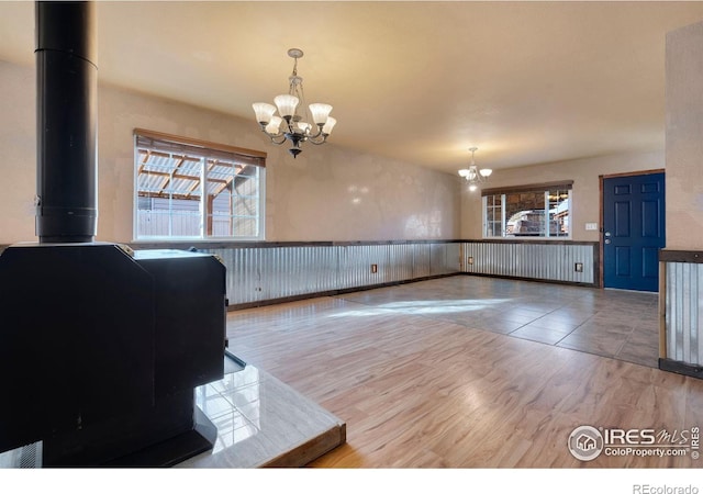 unfurnished dining area with wood-type flooring, a wood stove, and a notable chandelier