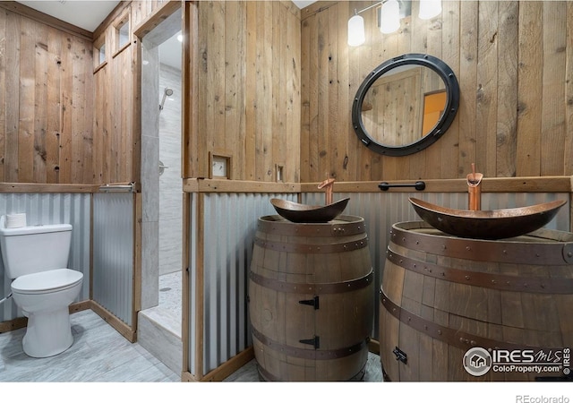 bathroom with sink, wood walls, and toilet