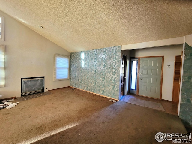 unfurnished living room featuring a tiled fireplace, vaulted ceiling, a textured ceiling, and carpet