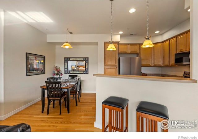 kitchen featuring a breakfast bar, decorative light fixtures, stainless steel refrigerator, kitchen peninsula, and light hardwood / wood-style floors