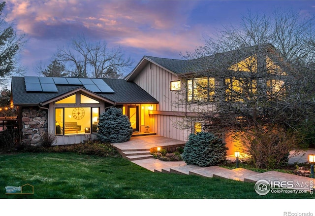 view of front of home with board and batten siding, a shingled roof, roof mounted solar panels, and a lawn