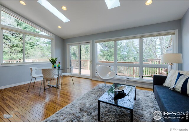 living room featuring lofted ceiling with skylight, baseboards, wood finished floors, and recessed lighting