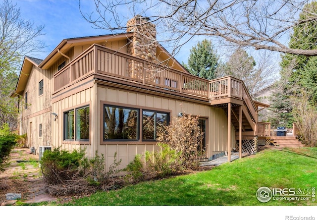 back of house featuring a chimney, a yard, stairs, a wooden deck, and board and batten siding