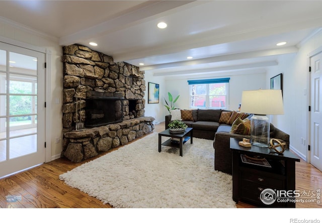 living area with crown molding, a fireplace, beam ceiling, and wood finished floors