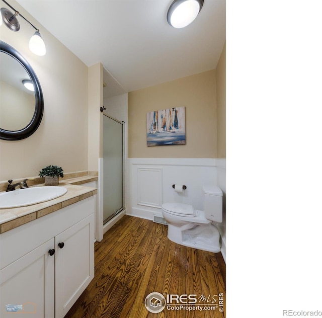 bathroom with toilet, wainscoting, vanity, a shower stall, and wood finished floors