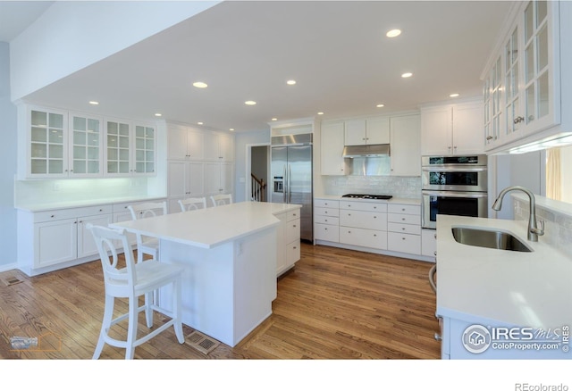 kitchen featuring a center island, stainless steel appliances, white cabinets, a sink, and under cabinet range hood