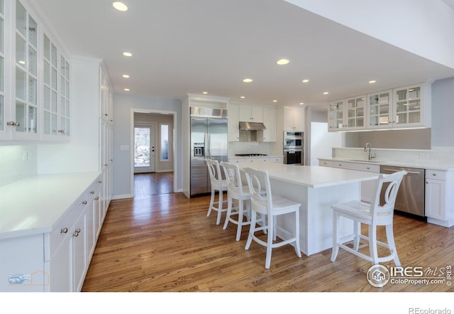 kitchen featuring under cabinet range hood, a sink, appliances with stainless steel finishes, a center island, and a kitchen bar