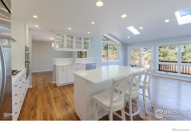 kitchen featuring lofted ceiling with skylight, glass insert cabinets, a breakfast bar, stainless steel appliances, and a sink