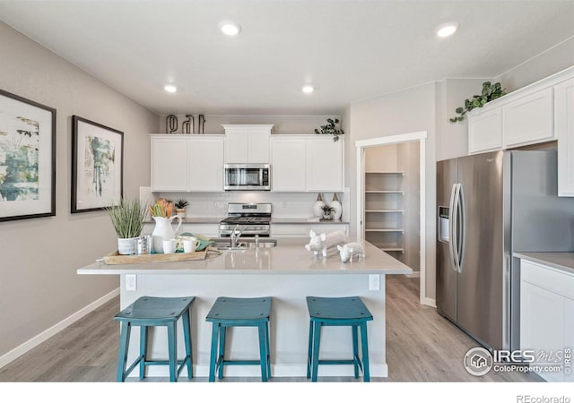 kitchen with white cabinetry, tasteful backsplash, light hardwood / wood-style flooring, stainless steel appliances, and a kitchen island with sink