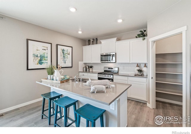 kitchen with appliances with stainless steel finishes, a center island with sink, white cabinets, and a kitchen bar