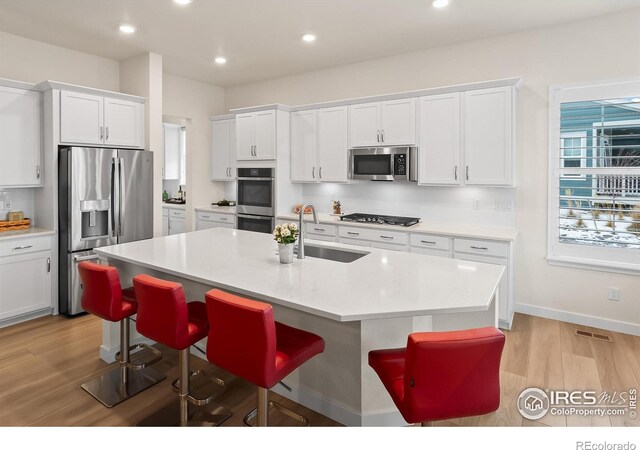 kitchen with a breakfast bar, sink, white cabinetry, appliances with stainless steel finishes, and an island with sink