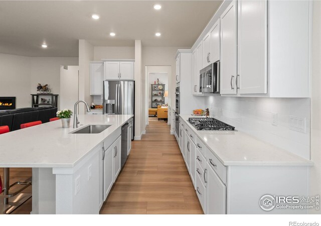 kitchen featuring sink, light stone counters, stainless steel appliances, a kitchen island with sink, and white cabinets