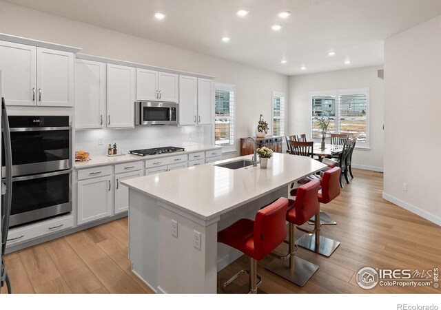 kitchen featuring sink, a breakfast bar, a kitchen island with sink, stainless steel appliances, and white cabinets