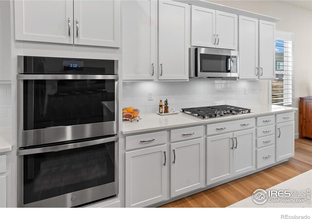 kitchen with backsplash, light hardwood / wood-style floors, white cabinets, and appliances with stainless steel finishes