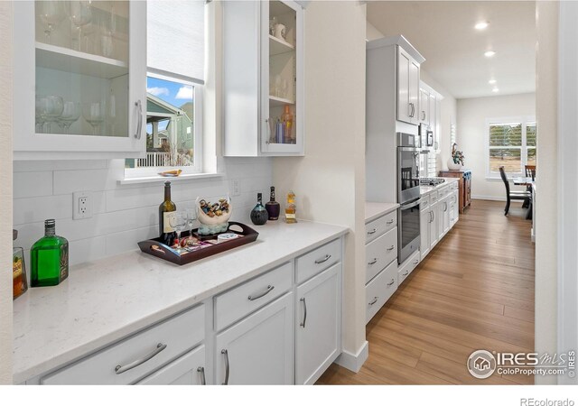 kitchen featuring tasteful backsplash, white cabinets, light stone countertops, stainless steel double oven, and light hardwood / wood-style flooring