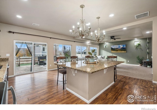 kitchen featuring dark hardwood / wood-style floors, decorative light fixtures, a breakfast bar area, a center island, and light stone counters