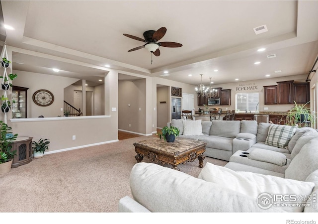 living room with light colored carpet, a raised ceiling, and ceiling fan with notable chandelier