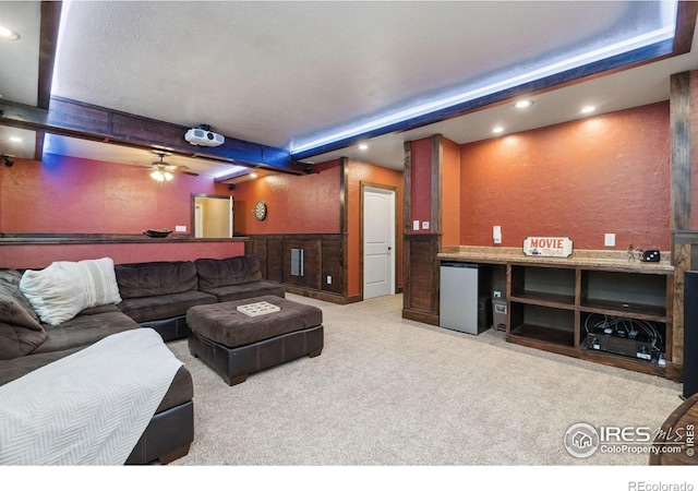 cinema room with beam ceiling, light carpet, and ceiling fan