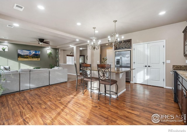 kitchen with hardwood / wood-style floors, a kitchen breakfast bar, hanging light fixtures, light stone counters, and stainless steel appliances